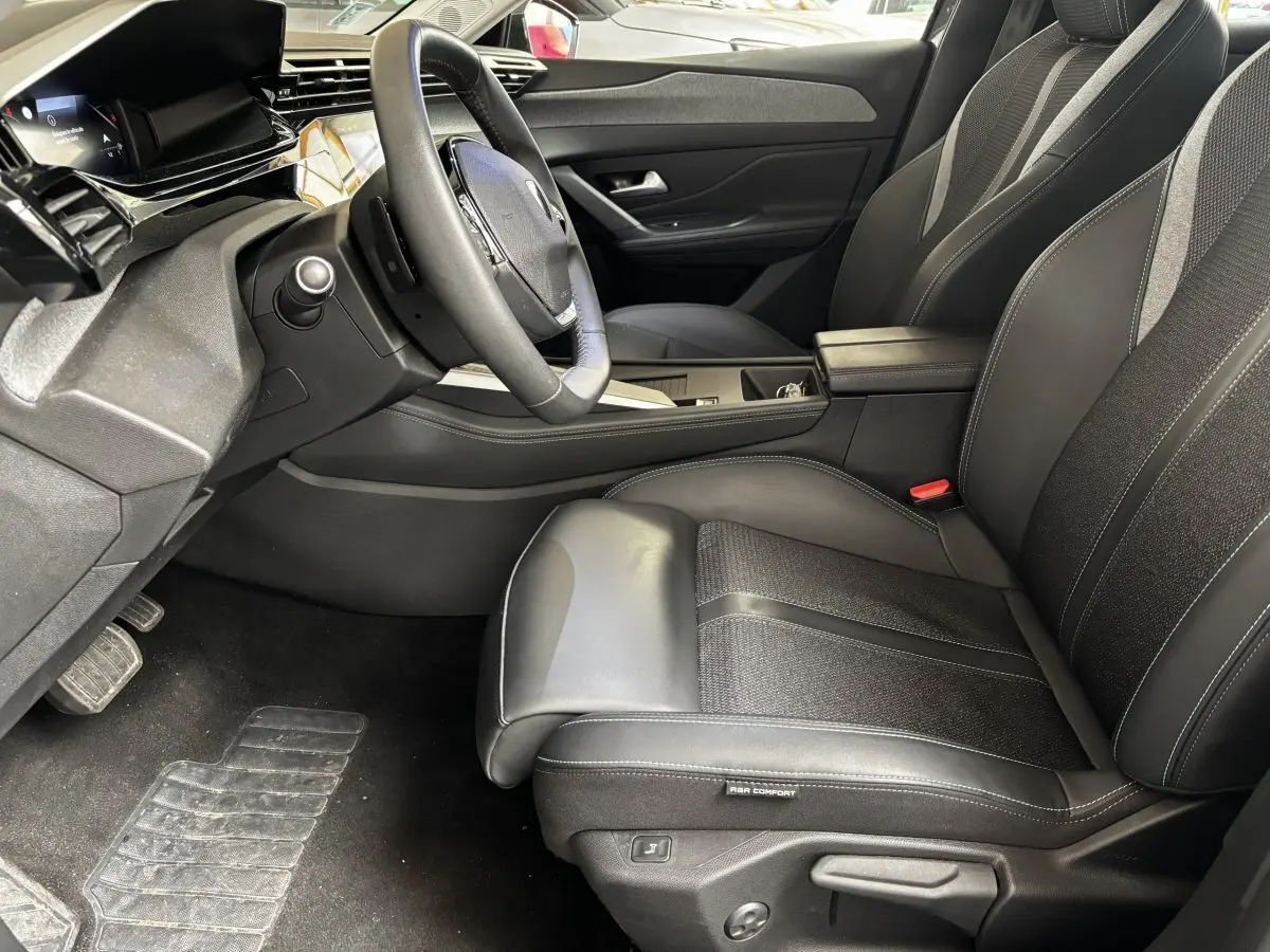 Intérieur avant droit de la Peugeot 308 gris clair 2024, siège en cuir noir avec volant multifonction et écran tactile.