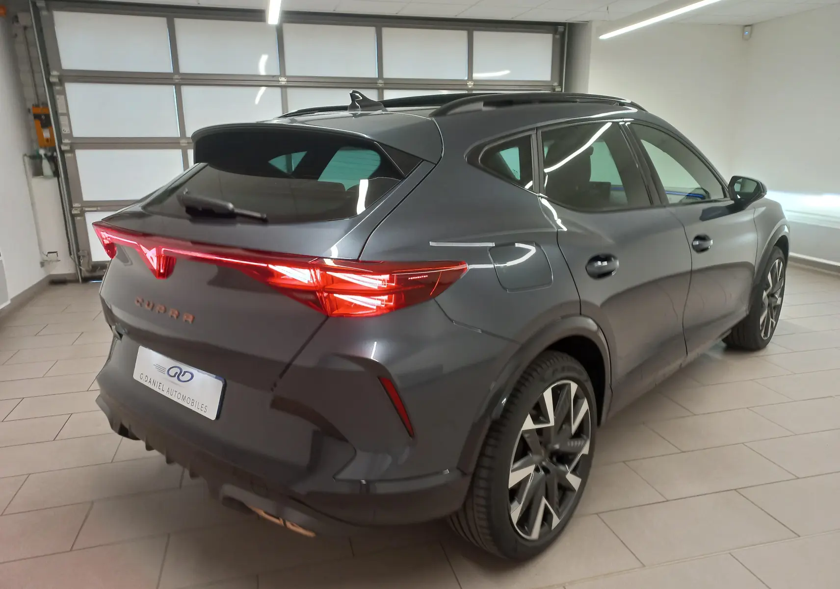 Vue 3/4 arrière droit du CUPRA Formentor gris magnétique avec toit ouvrant panoramique dans un garage.