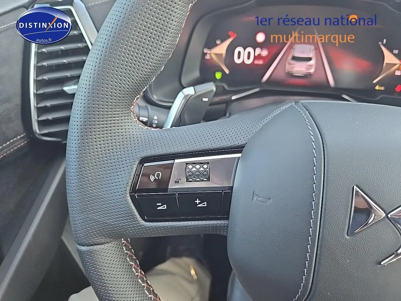 Gros plan sur le volant en cuir perforé gris du DS7 Cristal Pearl, avec commandes intégrées et tableau de bord numérique visible.