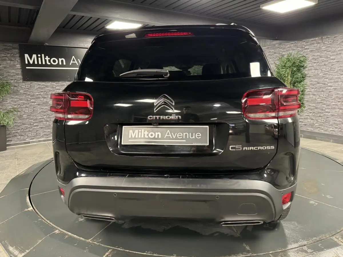 Vue arrière d'un Citroën C5 Aircross noir perla nera avec feux arrière LED et logo distinctif sur fond de showroom.