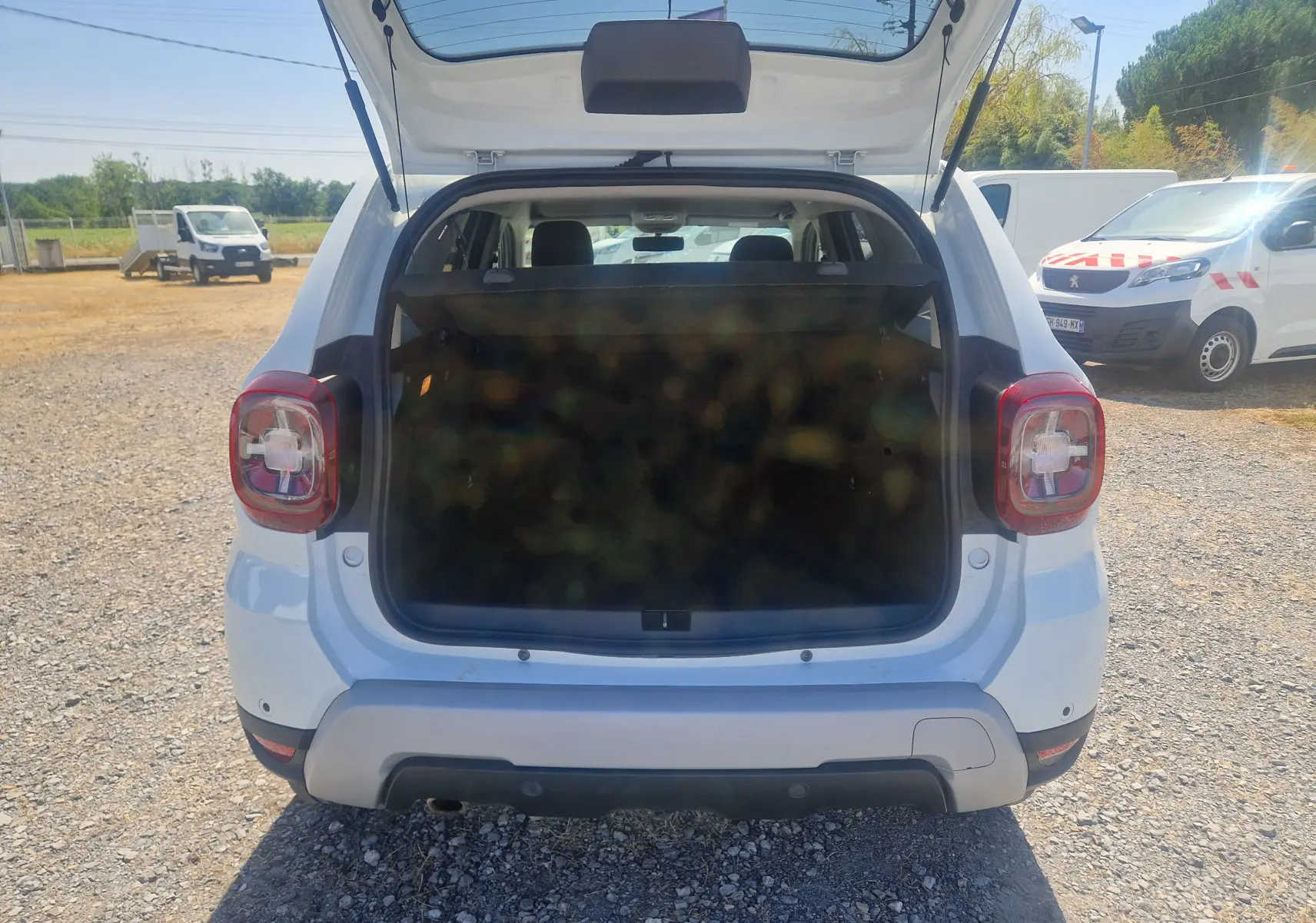Vue arrière ouverte du Dacia Duster blanc 2021, coffre spacieux visible avec hayon relevé en extérieur.
