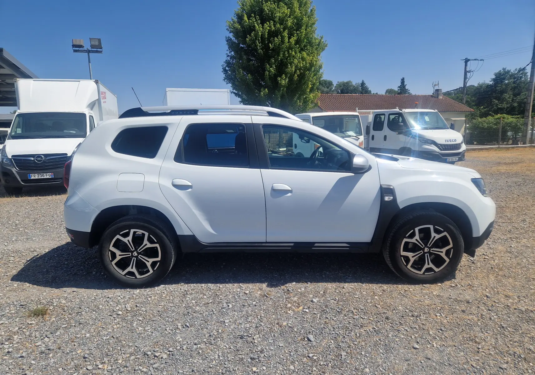 Profil côté gauche d'un Dacia Duster blanc 2021, version 4x2 Prestige avec jantes alliage noires et toit noir.
