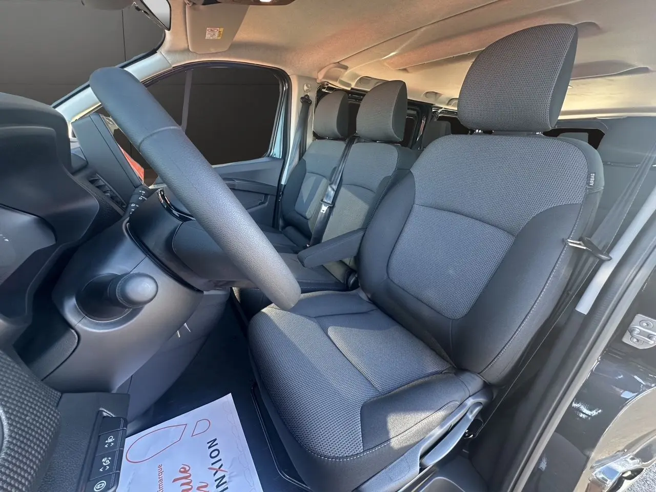 Intérieur avant droit du Renault Trafic Combi gris comète, montrant les sièges tissu noir et le volant.