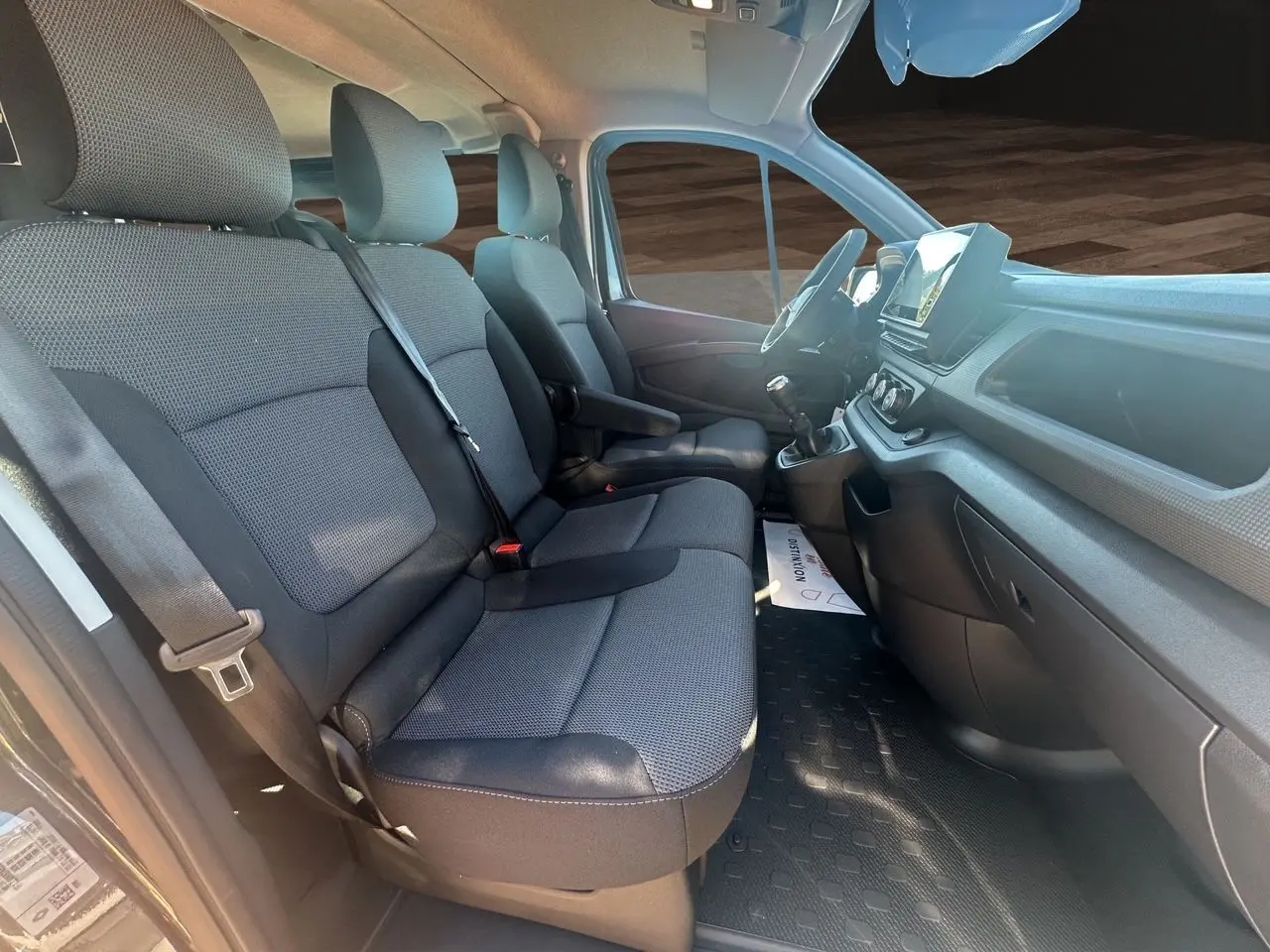 Vue intérieure côté conducteur du Renault Trafic Combi 2025, sièges tissu noir et tableau de bord avec écran tactile.