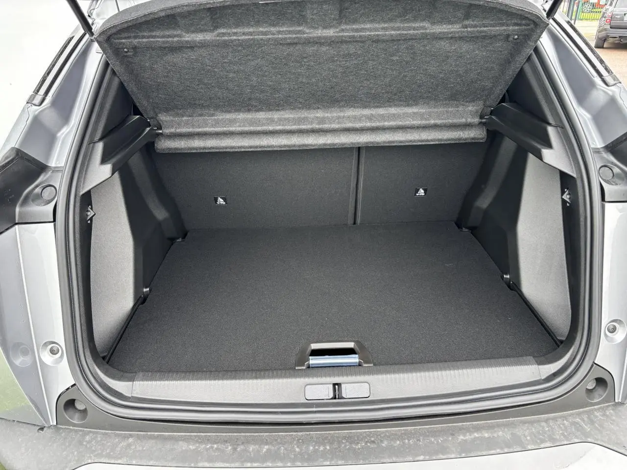 Coffre ouvert vu de l'arrière du Peugeot 2008 gris Artense avec intérieur noir et cache-bagages relevé.