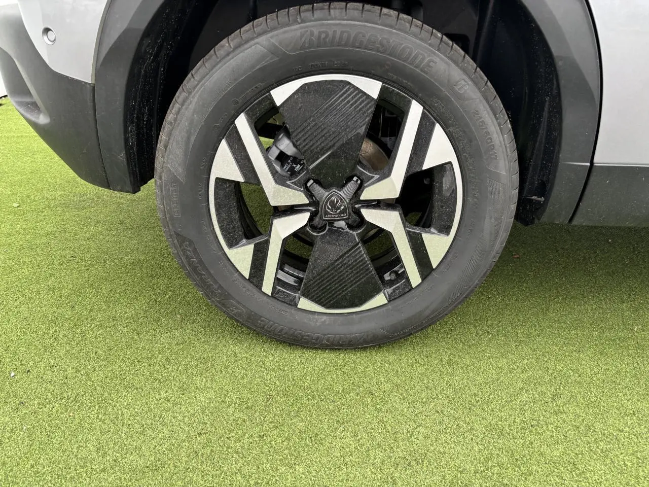 Gros plan sur la roue avant droite du Peugeot 2008 gris Artense avec jante alliage bi-ton noir et argent.