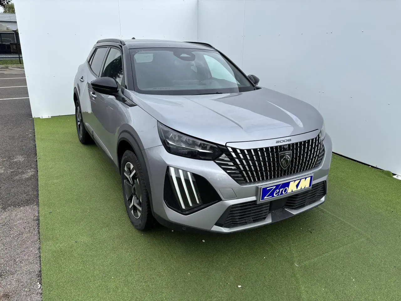 Peugeot 2008 gris Artense toit noir en 3/4 avant droit, calandre noire à liserés chromés et feux LED griffés visibles.