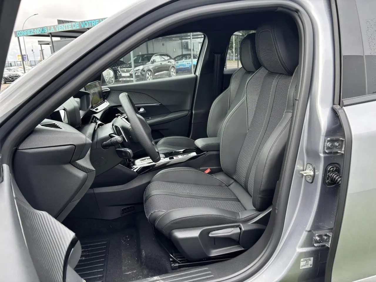 Vue intérieure côté conducteur du Peugeot 2008 gris Artense, sièges tissu et cuir avec surpiqûres vertes et volant compact cuir.
