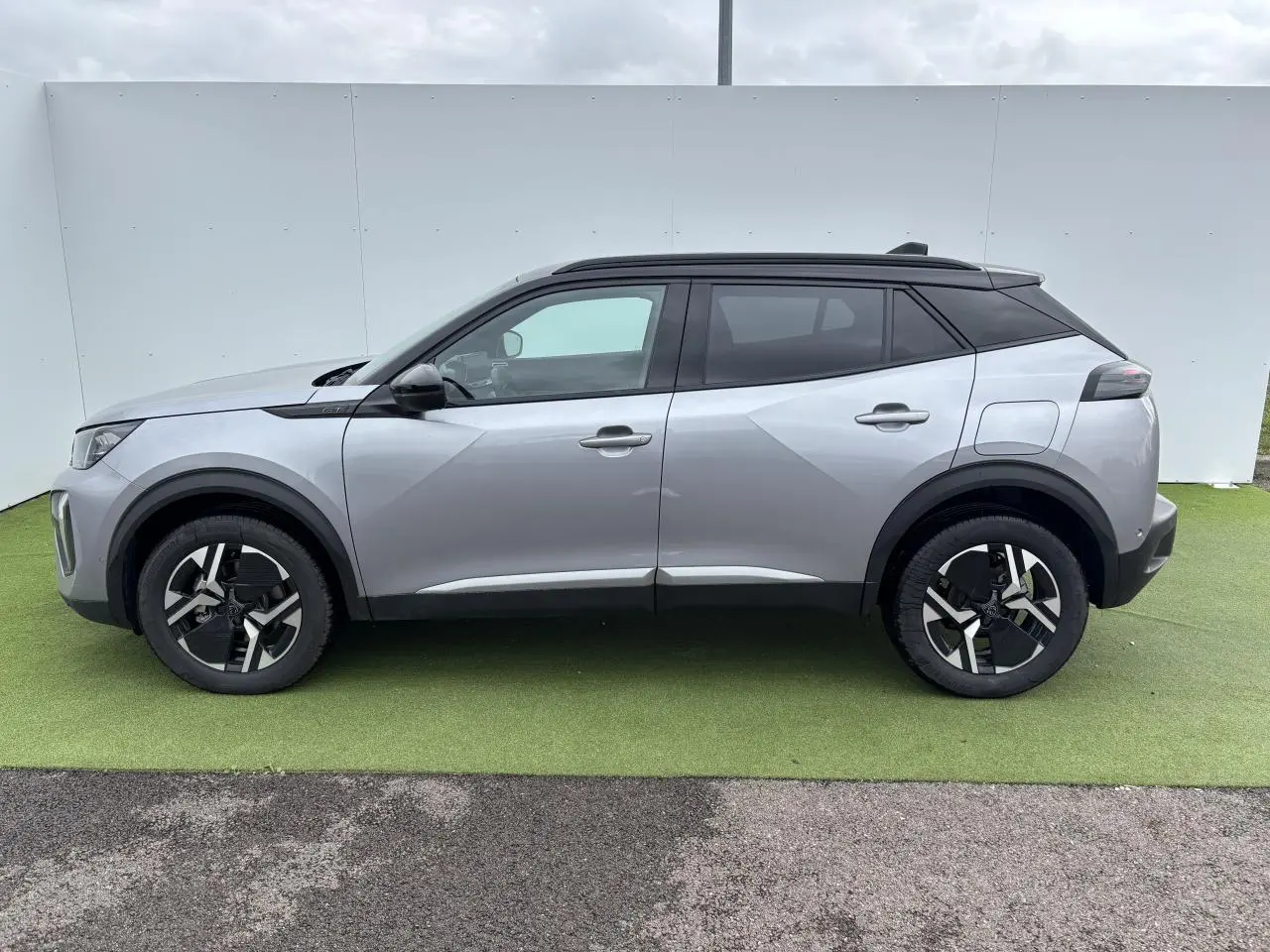 Profil côté gauche du Peugeot 2008 gris Artense avec toit noir, jantes bi-ton et lignes anguleuses modernes.
