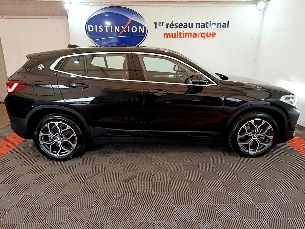 Profil droit d’un BMW X2 sDrive18i Lounge noir 2023 en intérieur avec jantes alliage et logo BMW visible sur l’aile arrière.