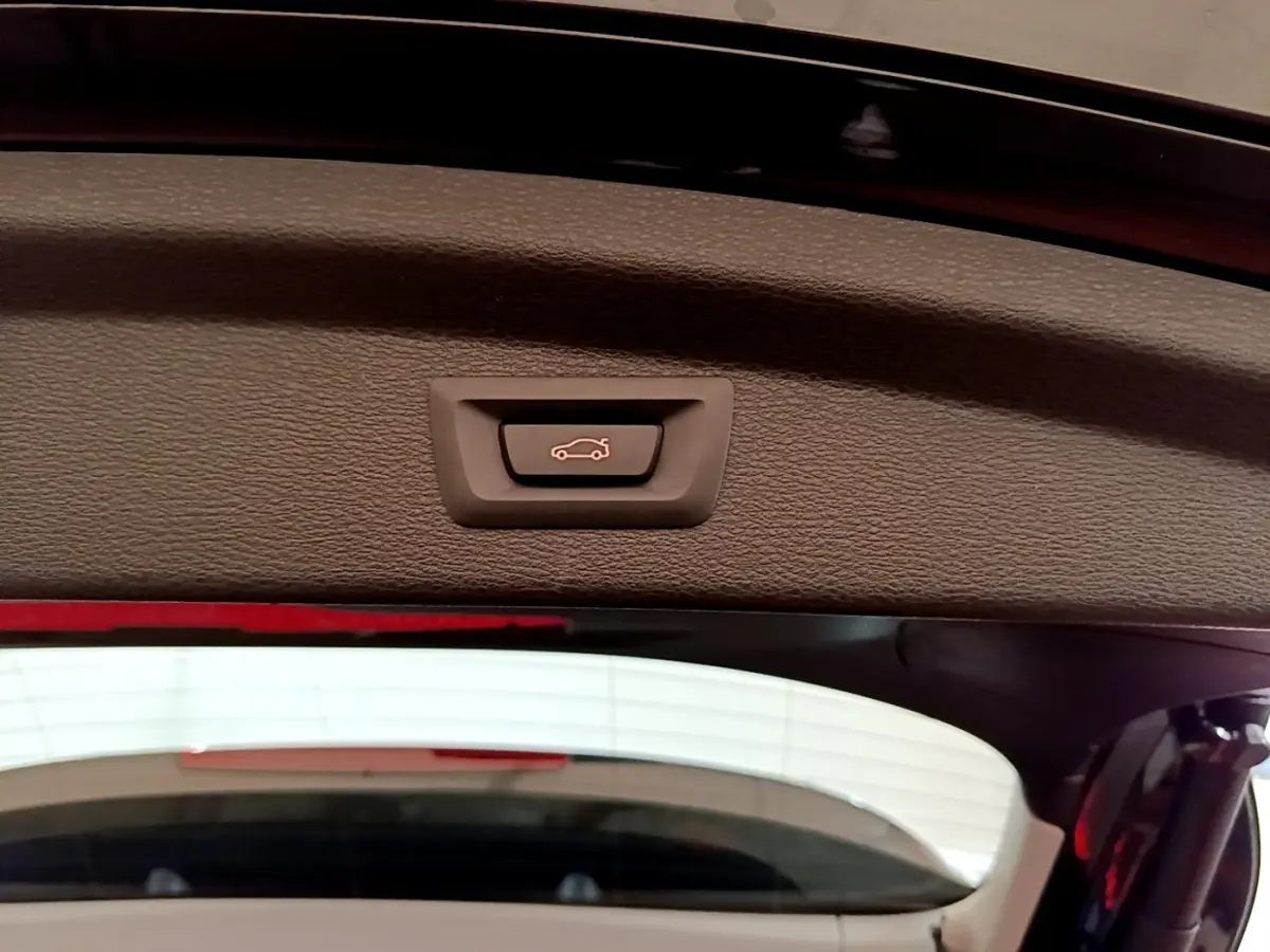 Bouton d'ouverture électrique du coffre sur la partie intérieure du hayon d'une BMW X2 noire vue de l'arrière.