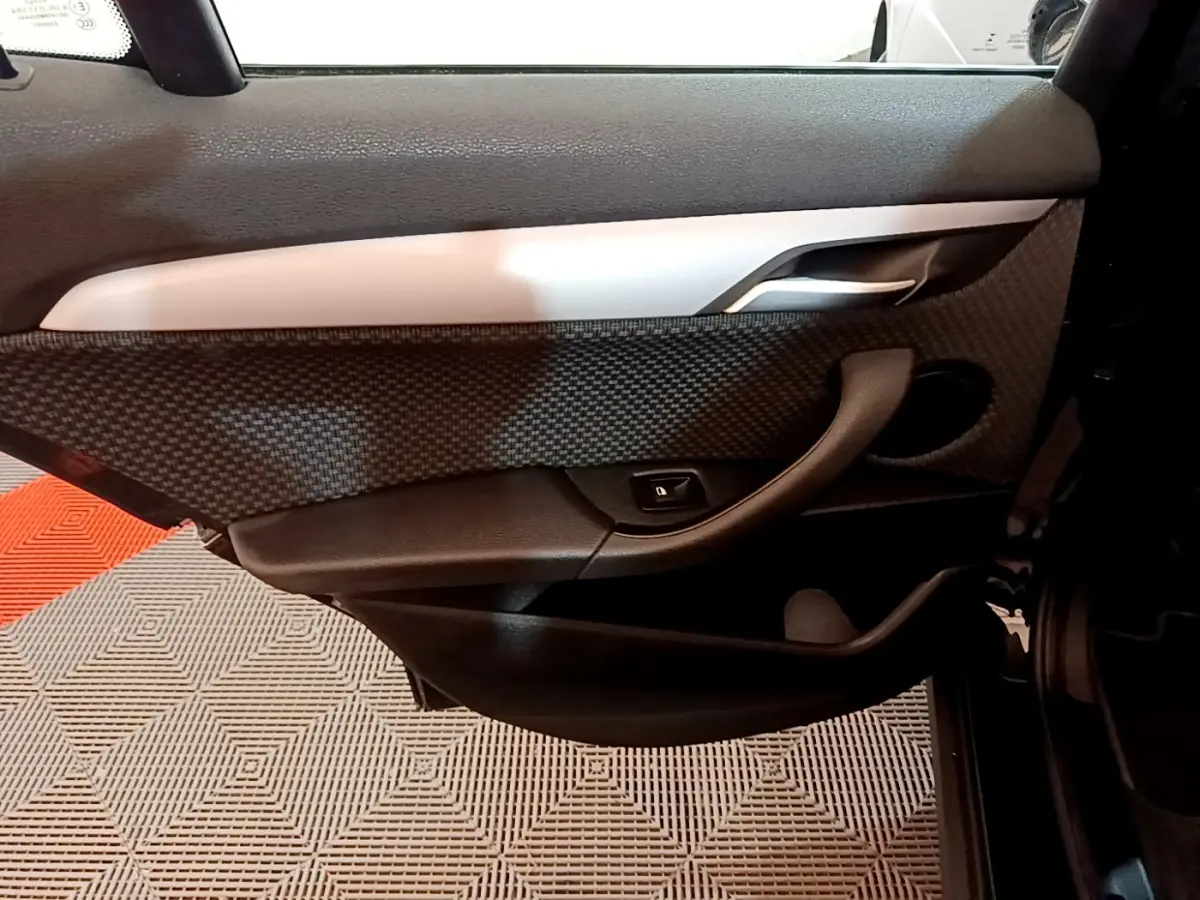 Vue intérieure côté gauche de la porte arrière noire de BMW X2 sDrive18i Lounge avec insert carbone et poignée argentée.