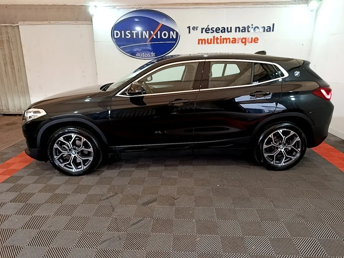 Profil droit d’un BMW X2 sDrive18i Lounge noir 2023, avec jantes alliage et feux arrière LED visibles en intérieur showroom.