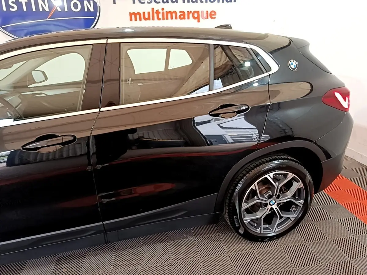 Vue latérale droite du BMW X2 sDrive18i Lounge noir, mettant en valeur la jante alliage et le logo BMW arrière.