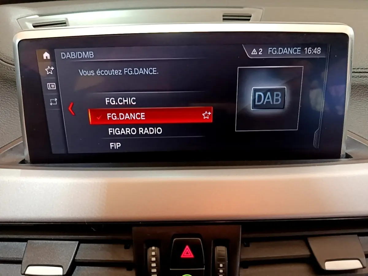 Écran central du tableau de bord du BMW X2 sDrive18i Lounge 2023 affichant la radio DAB en mode FG.DANCE.