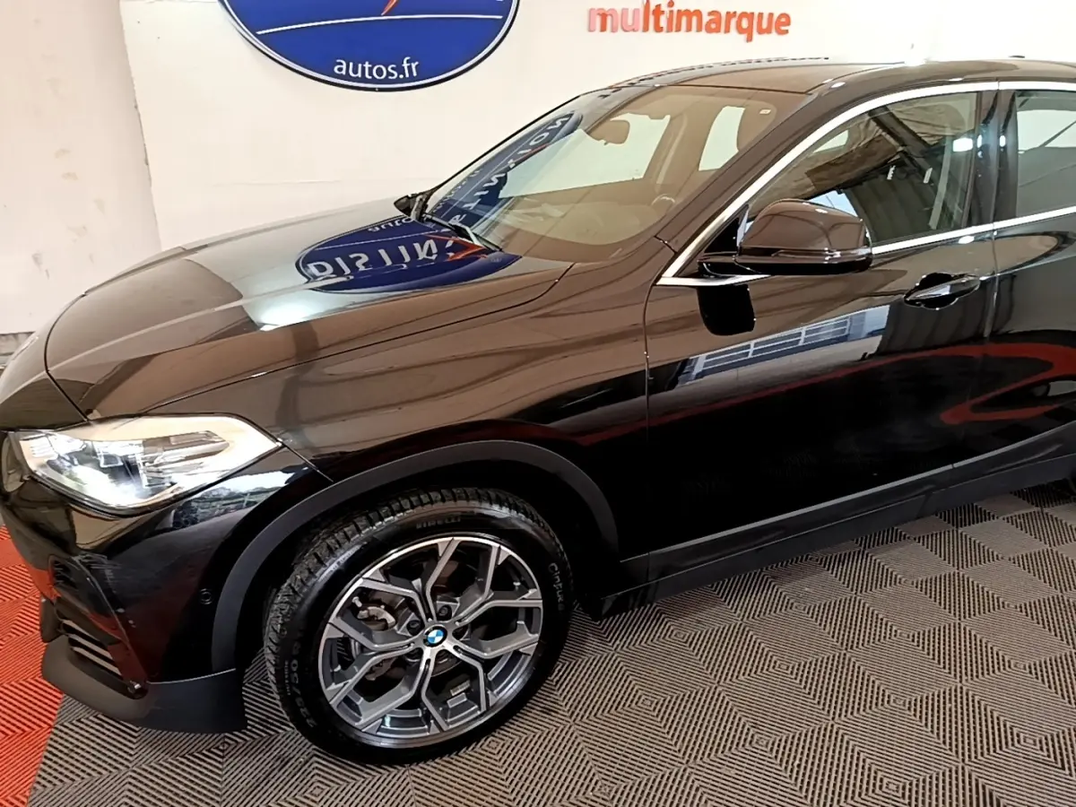 BMW X2 sDrive18i Lounge noir vue 3/4 avant droit, mettant en valeur les jantes alliage et les phares LED distinctifs.