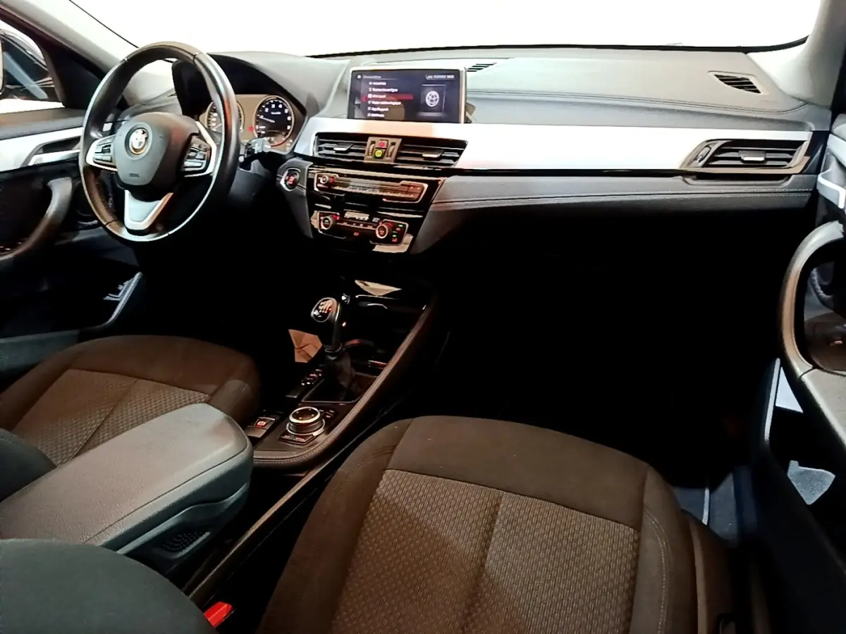 Vue intérieure avant droite du BMW X2 sDrive18i Lounge 2023, montrant le tableau de bord et la console centrale avec boîte manuelle.