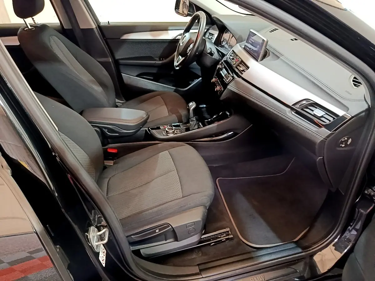 Vue intérieure côté conducteur de la BMW X2 sDrive18i Lounge 2023 noire, avec tableau de bord et console centrale visibles.