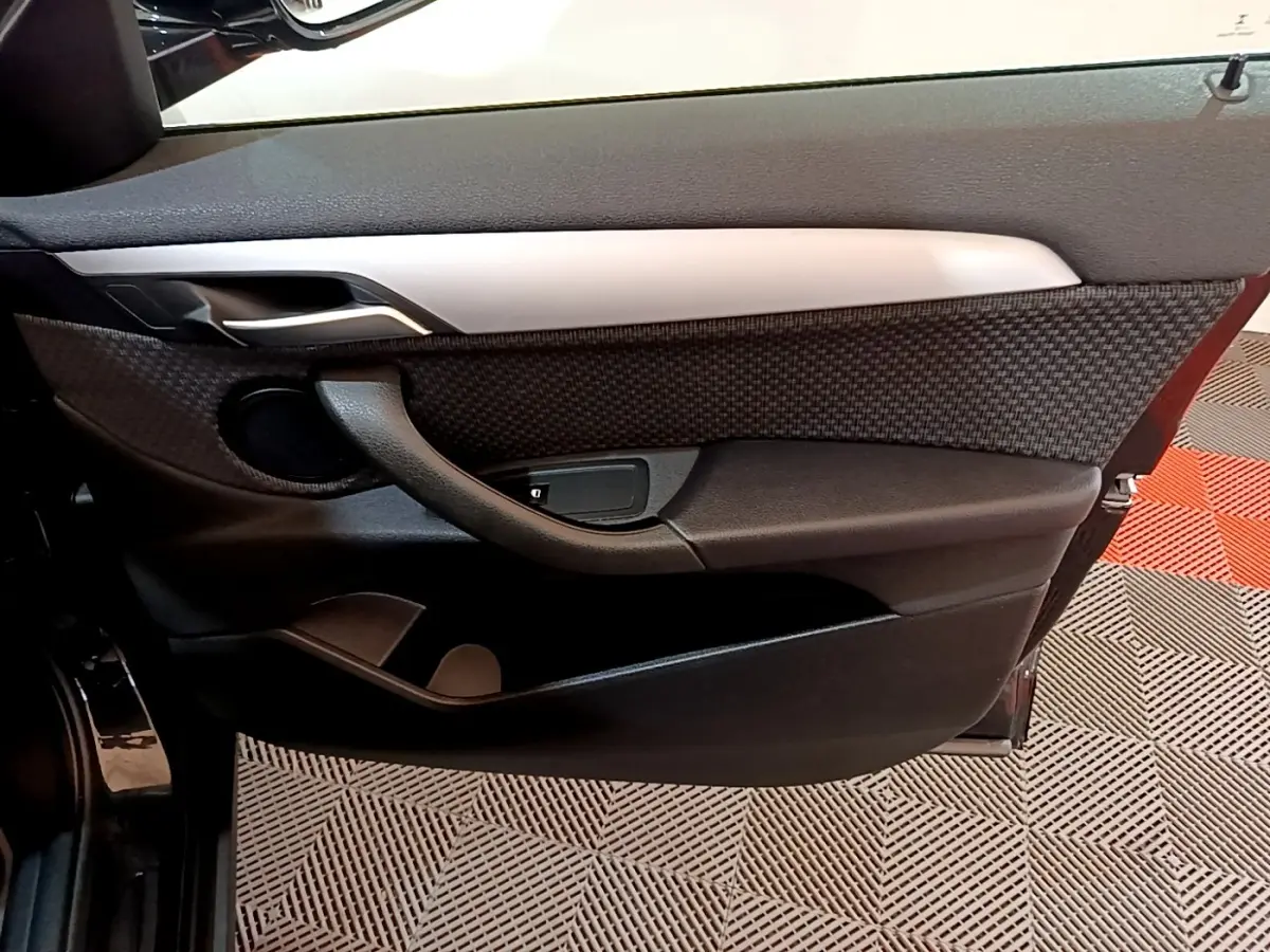 Vue intérieure de la porte avant gauche noire de la BMW X2 sDrive18i Lounge 2023 avec habillage texturé et poignée intégrée.