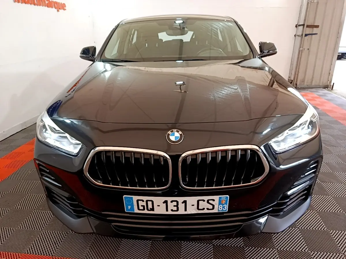 Vue avant rapprochée d’un BMW X2 sDrive18i Lounge noir avec calandre double haricot et phares LED allumés.