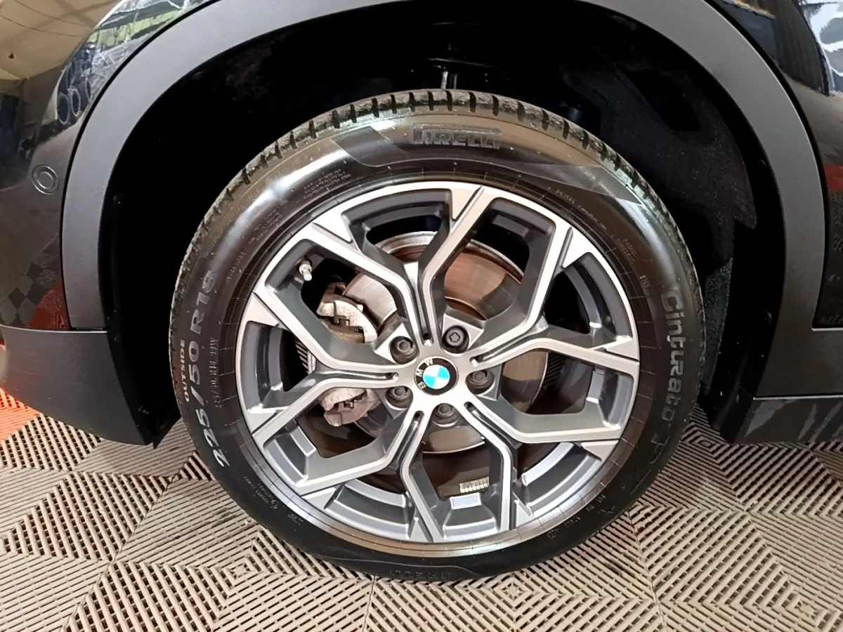 Gros plan sur la roue avant gauche noire d’un BMW X2 sDrive18i Lounge avec jante alliage gris et logo BMW central.