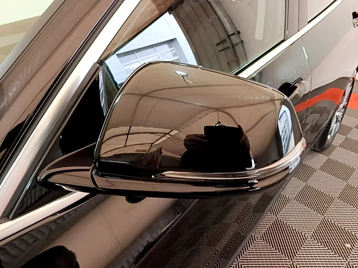 Gros plan sur le rétroviseur côté gauche noir brillant d’une BMW X2 sDrive18i Lounge 2023 avec reflet de l’environnement intérieur.