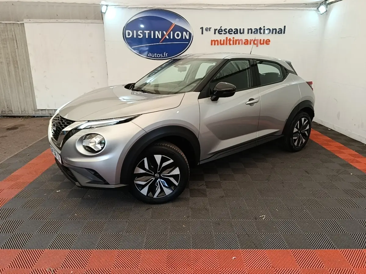 Nissan Juke gris clair en 3/4 avant droit, avec jantes noires et grises, dans un showroom intérieur.