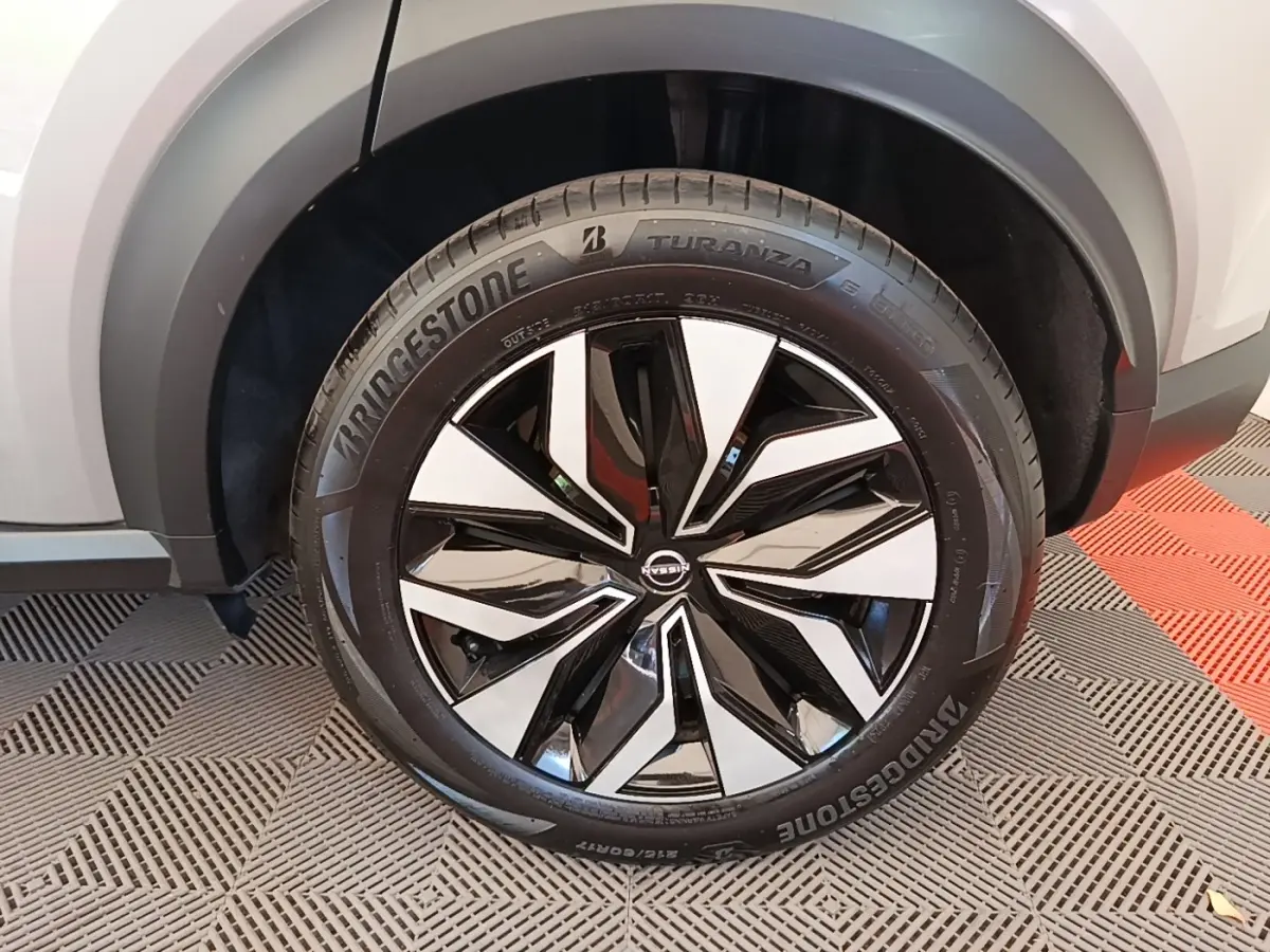 Gros plan sur la roue avant droite du Nissan Juke gris clair 2023 avec jante alliage bicolore et pneu Bridgestone.