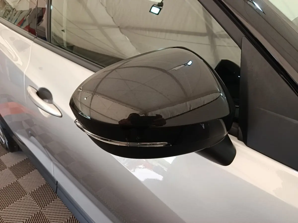 Rétroviseur côté gauche noir brillant sur Nissan Juke gris clair, vue rapprochée du côté conducteur.