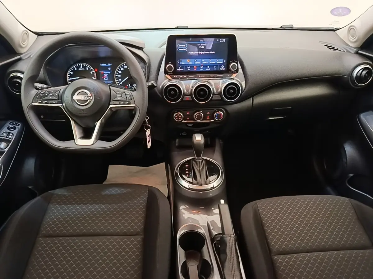 Vue intérieure avant du Nissan Juke 2023 essence, tableau de bord noir avec écran tactile central et volant multifonctions.