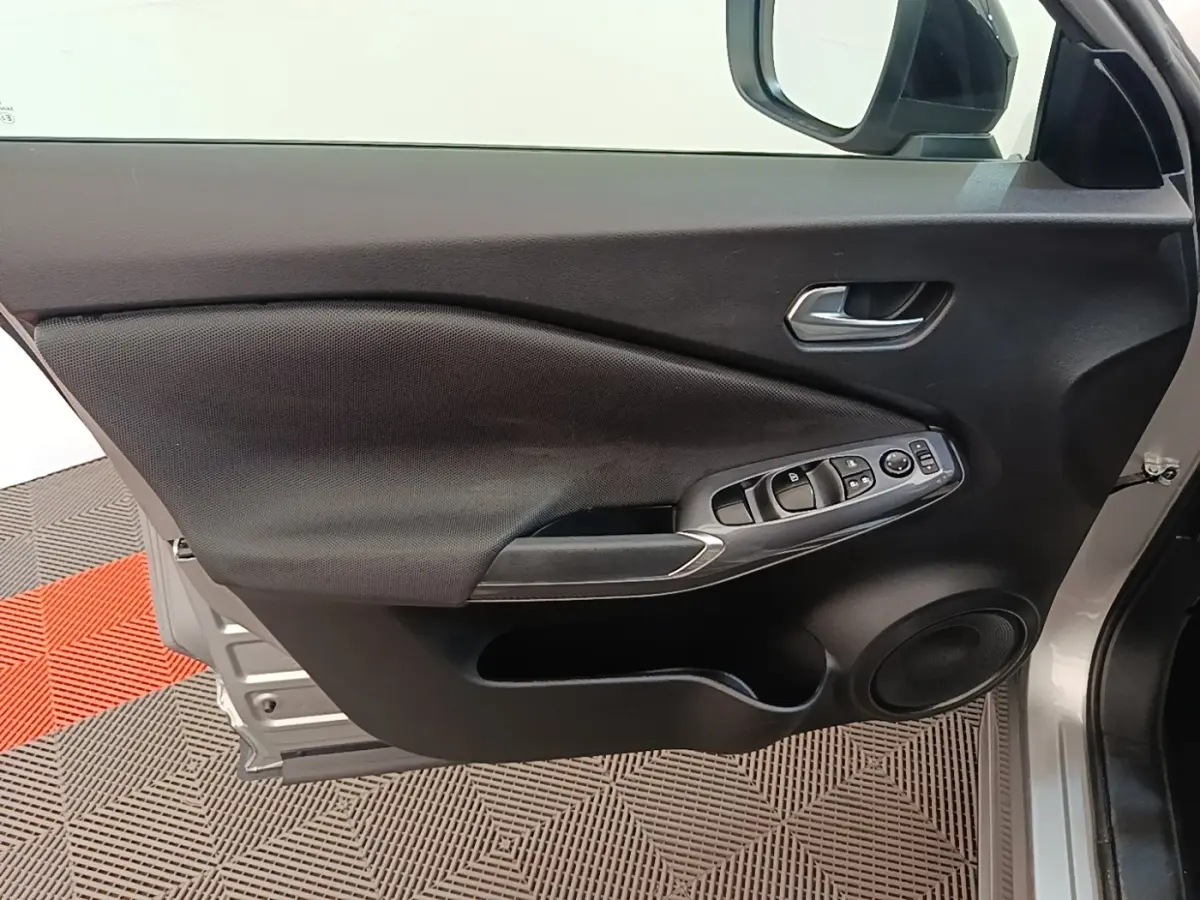 Vue intérieure de la porte avant gauche gris clair du Nissan Juke 2023 avec commandes électriques et haut-parleur intégré.