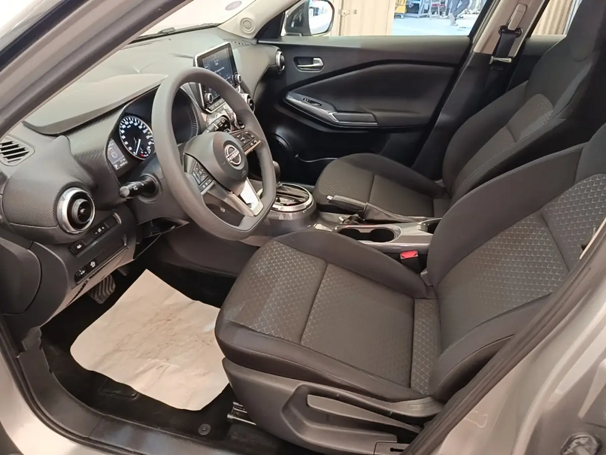 Vue intérieure côté conducteur du Nissan Juke gris clair 2023, avec tableau de bord digital et sièges tissu noirs.