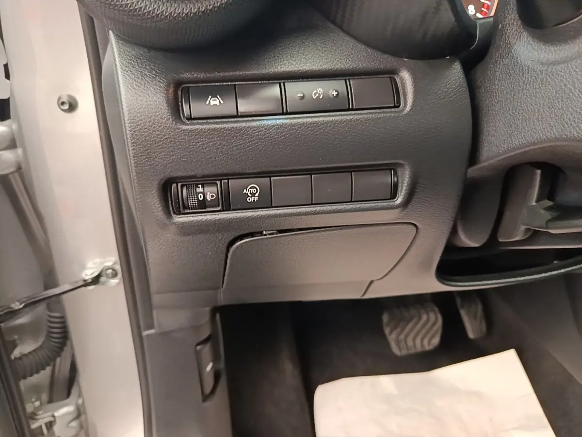 Détail du tableau de bord côté gauche avec commandes d'assistance et réglage des phares sur Nissan Juke gris clair 2023.