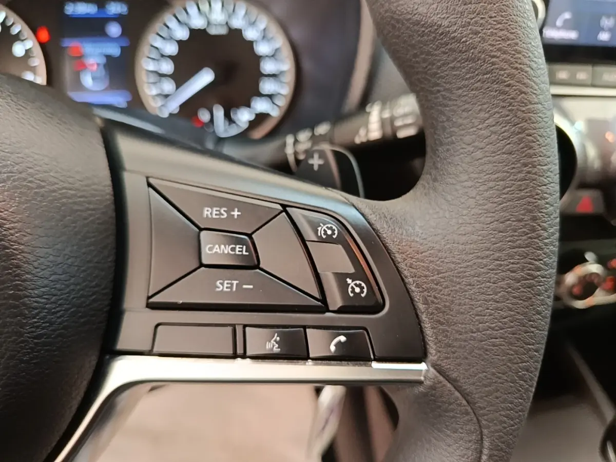 Gros plan sur les commandes du régulateur de vitesse au volant noir du Nissan Juke 2023, tableau de bord flou en arrière-plan.