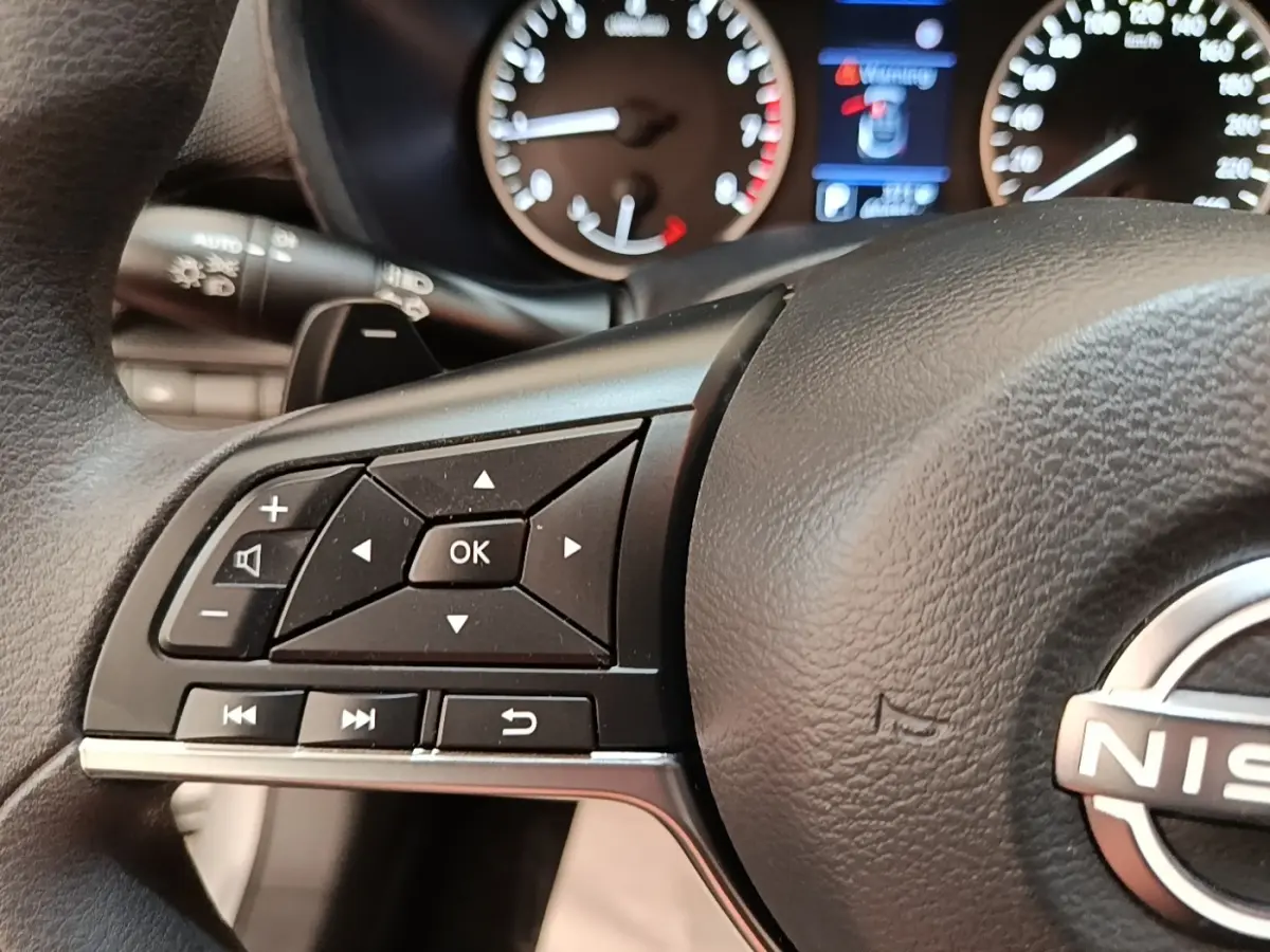 Gros plan sur le volant noir du Nissan Juke 2023 avec commandes multifonctions et tableau de bord en arrière-plan.