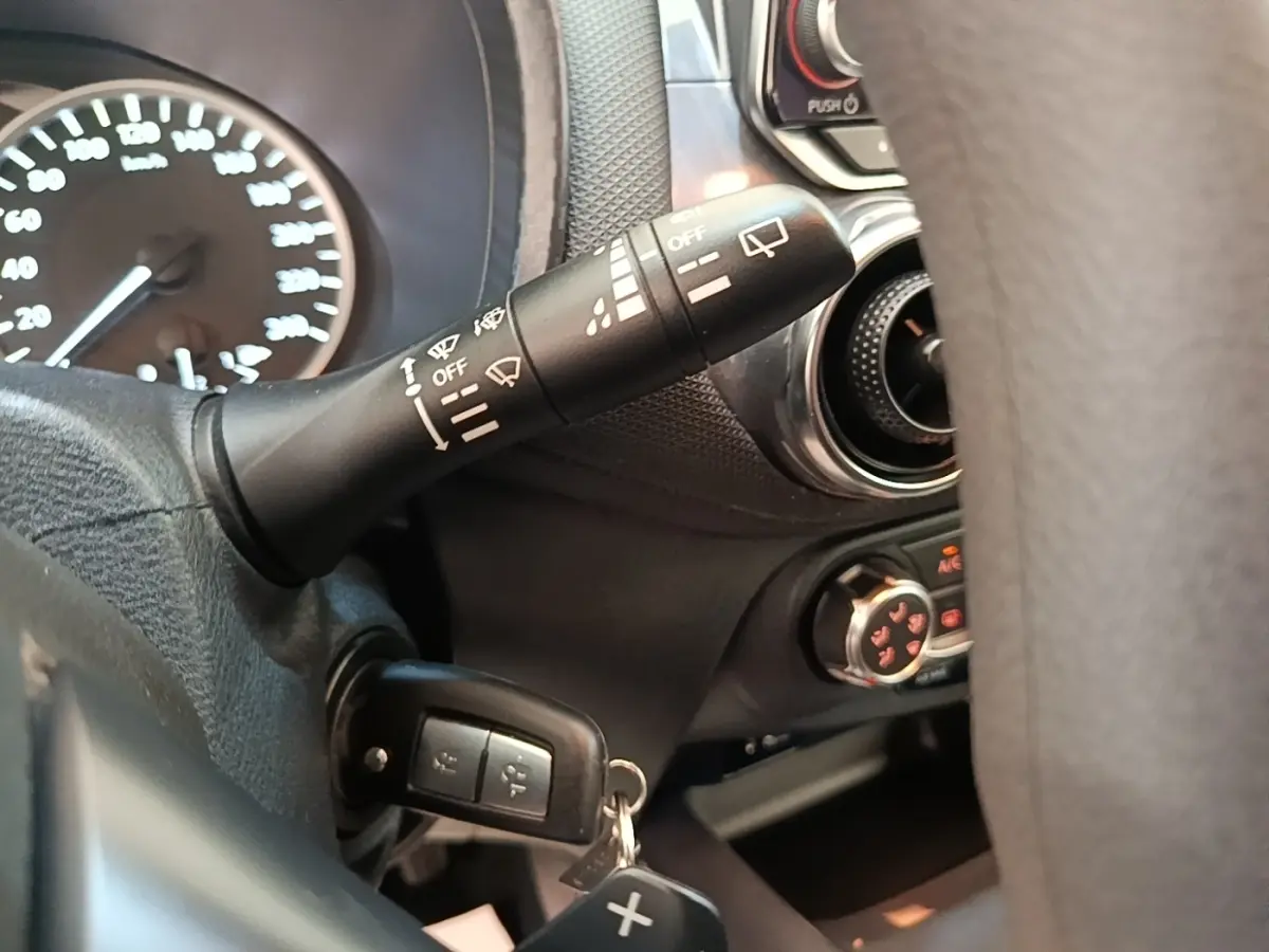 Gros plan intérieur sur la commande d’essuie-glace et le tableau de bord noir du Nissan Juke gris clair 2023.