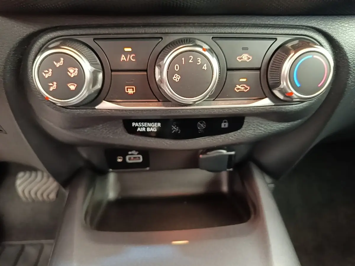 Détail du tableau de bord du Nissan Juke 2023 avec commandes climatisation, ports USB et prise 12V visibles.