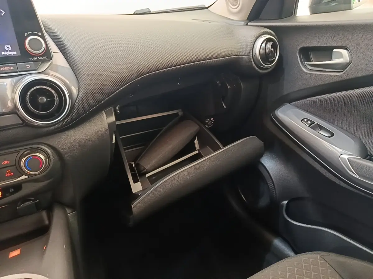Intérieur noir du Nissan Juke 2023, vue côté passager avec boîte à gants ouverte et tableau de bord visible.