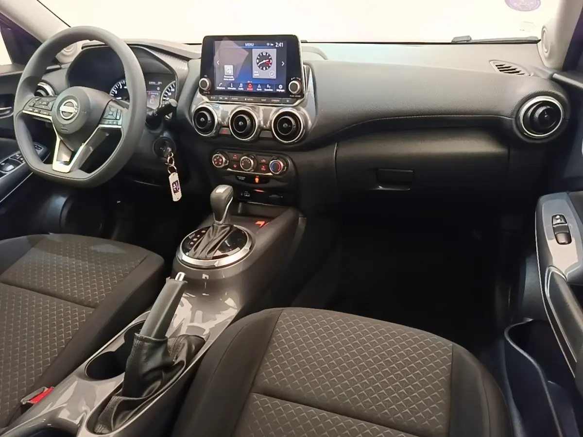 Vue intérieure avant du Nissan Juke gris clair 2023, avec tableau de bord central tactile et volant multifonctions.