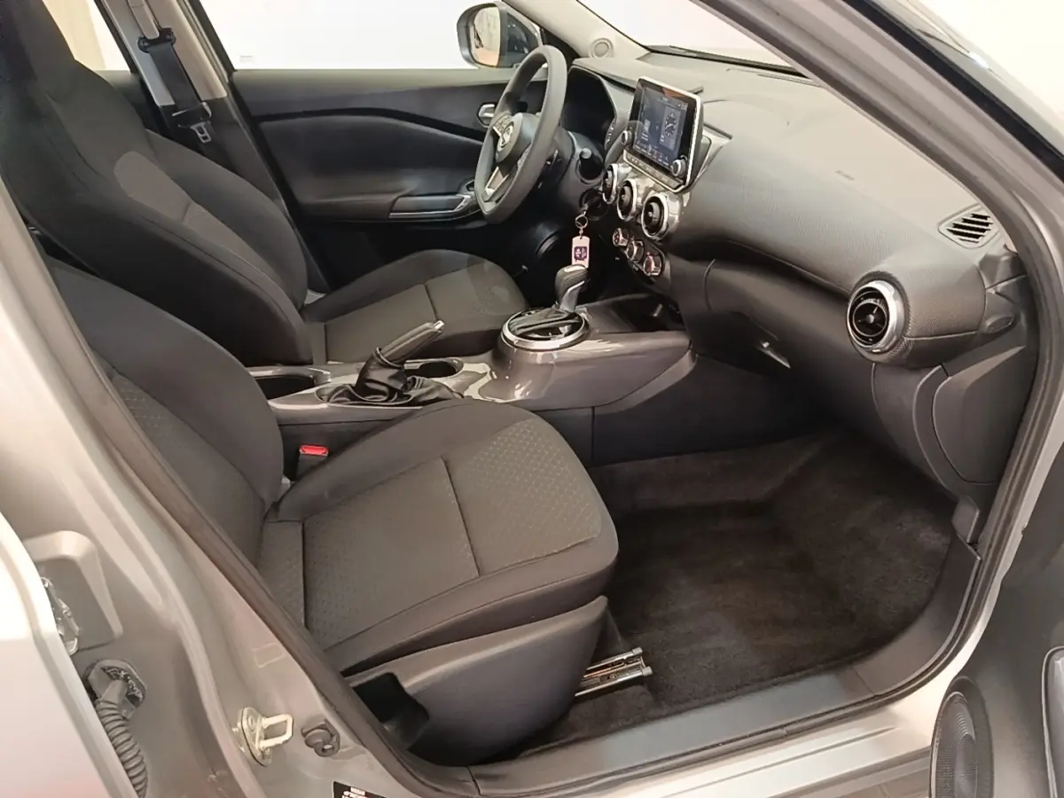Intérieur avant droit du Nissan Juke gris clair 2023, montrant sièges tissu noirs et tableau de bord avec écran tactile.