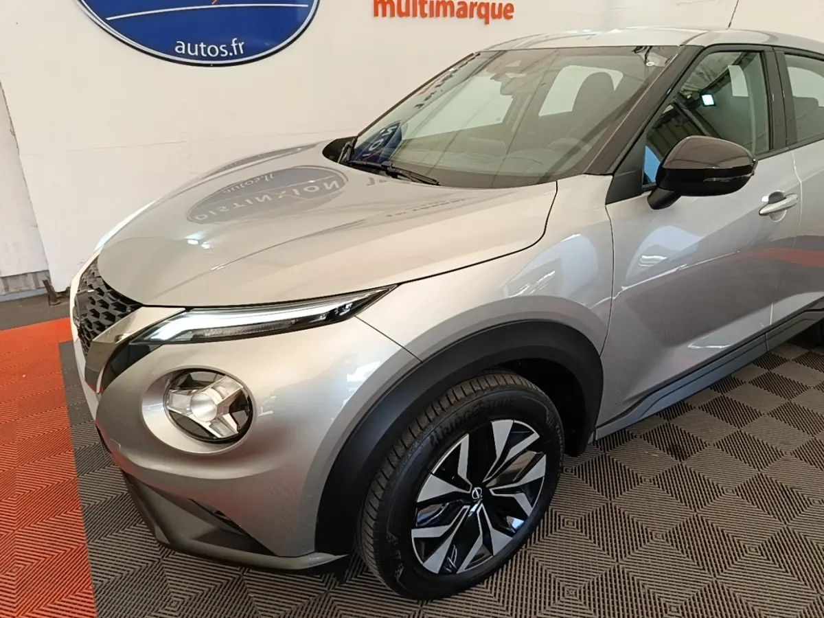 Nissan Juke gris clair en 3/4 avant droit, avec phares LED et jantes alliage bicolores visibles.