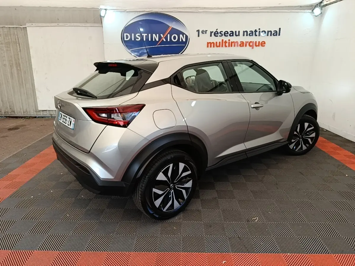 Nissan Juke gris clair en 3/4 arrière droit, avec toit noir et jantes alliage distinctives, stationné en intérieur.