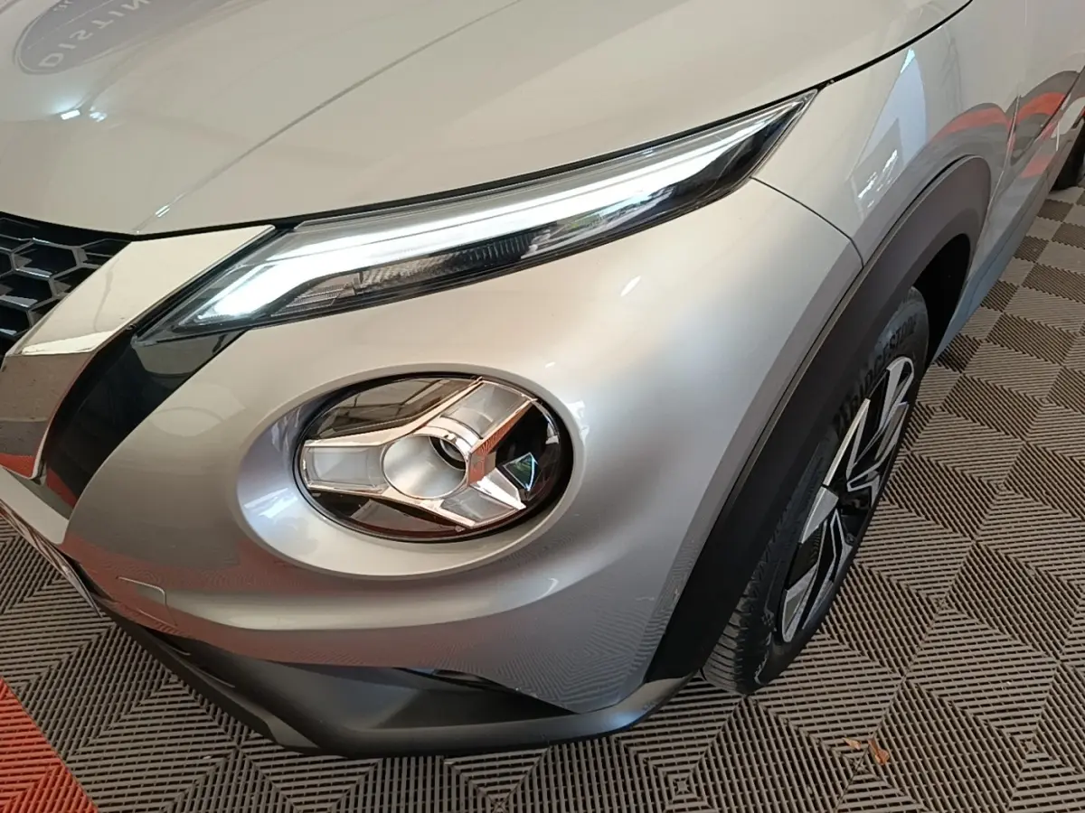 Gros plan sur l'avant droit gris clair du Nissan Juke 2023, mettant en valeur son phare LED et la jante stylisée.