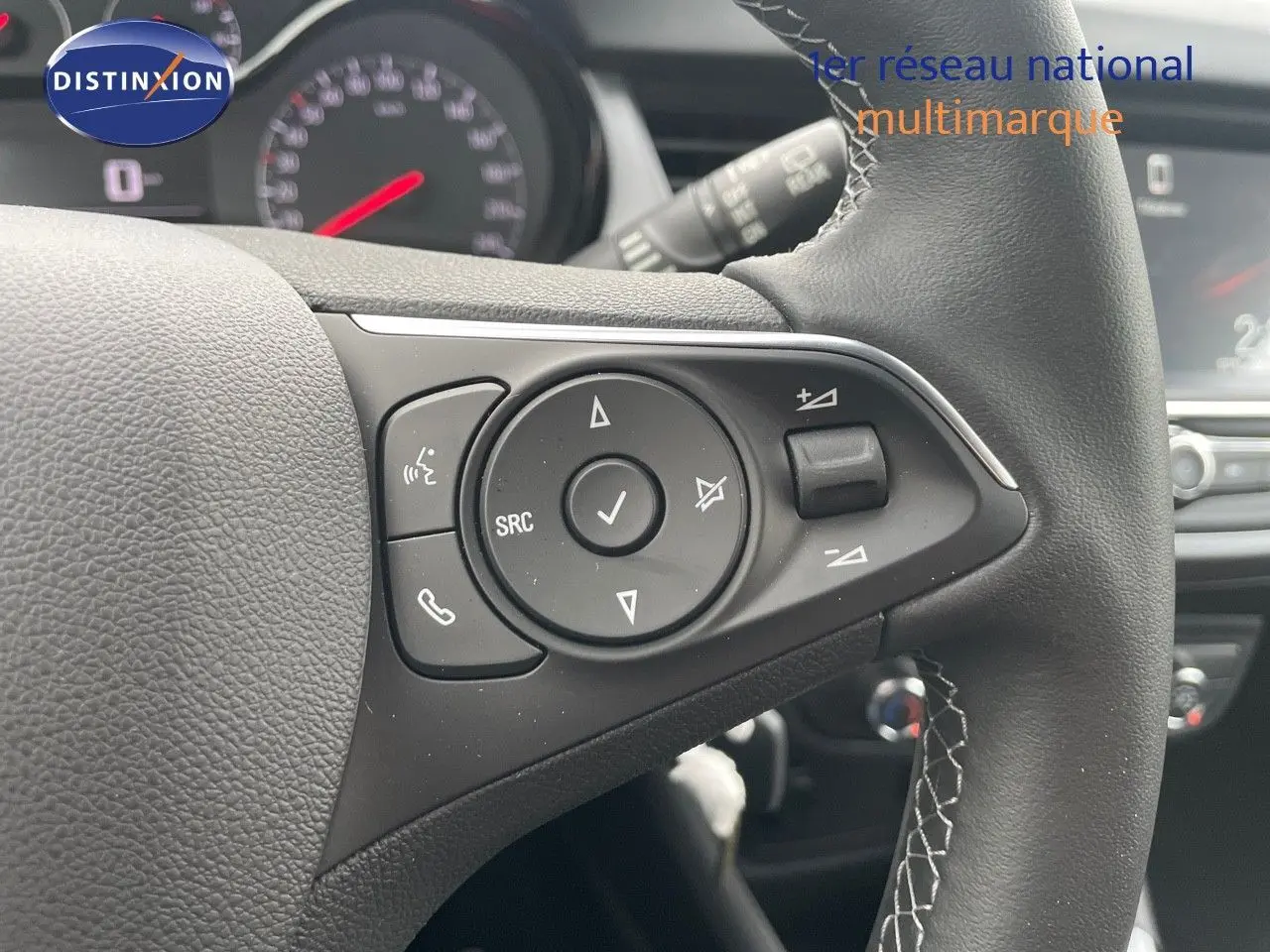 Gros plan sur les commandes du volant en cuir noir de l'Opel Crossland gris minéral, avec tableau de bord flou en arrière-plan.