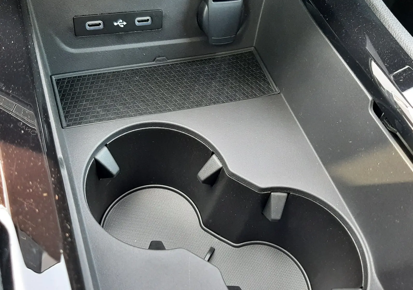 Gros plan sur la console centrale noire du Renault Espace VI hybride, montrant porte-gobelets et ports USB.