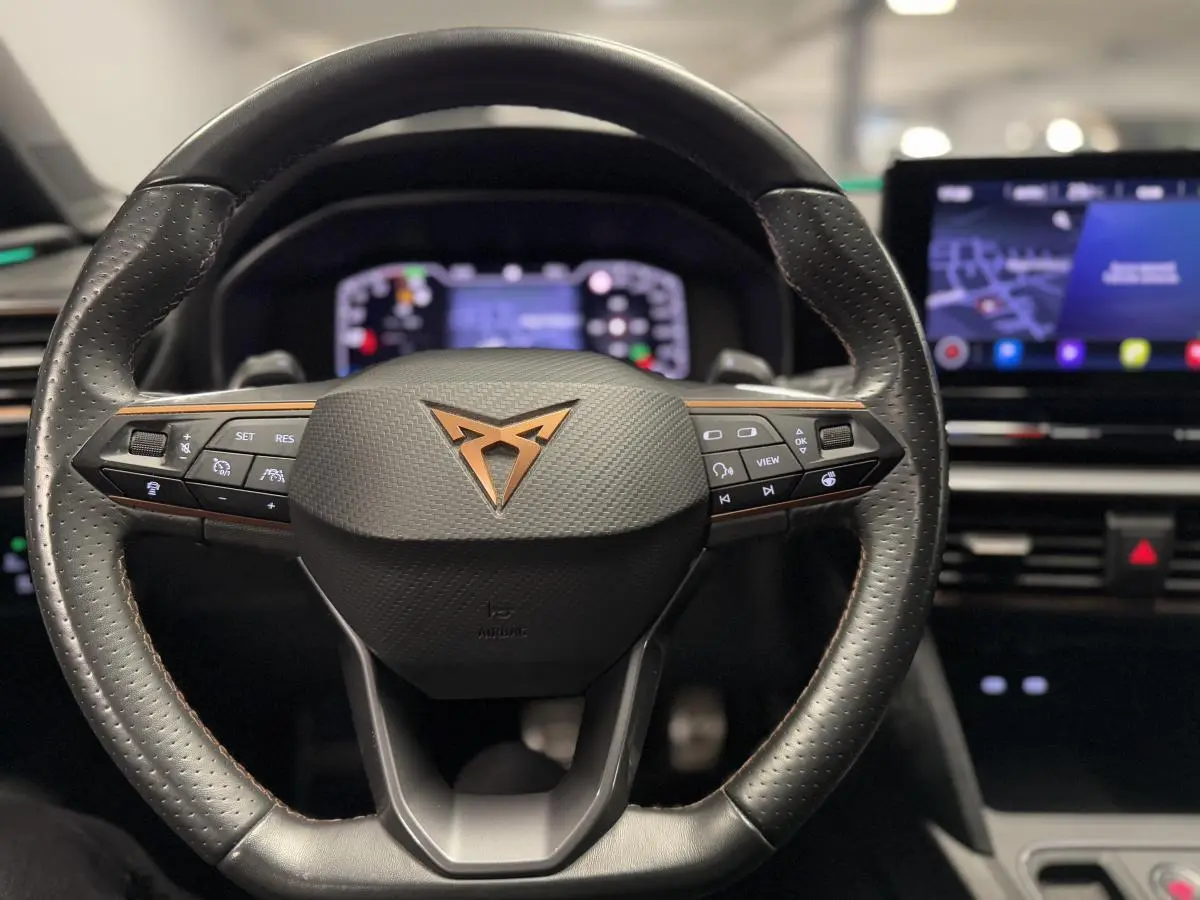 Volant en cuir perforé avec logo CUPRA cuivré, vue frontale sur le tableau de bord numérique et écran tactile du Leon Sportstourer rouge.