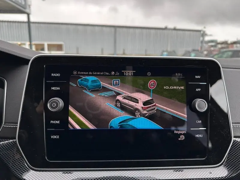 Écran central montrant l’aide à la conduite avec un Volkswagen T-Cross gris Ascot vu de trois quarts arrière droit.