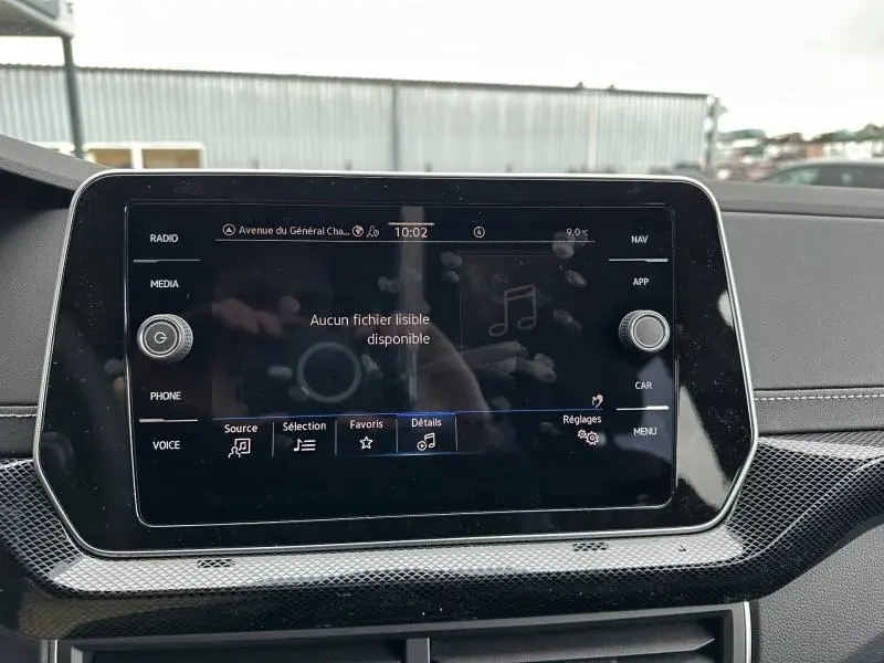 Écran tactile central du Volkswagen T-Cross 2025 affichant un menu multimédia, avec reflets et traces de doigts visibles.