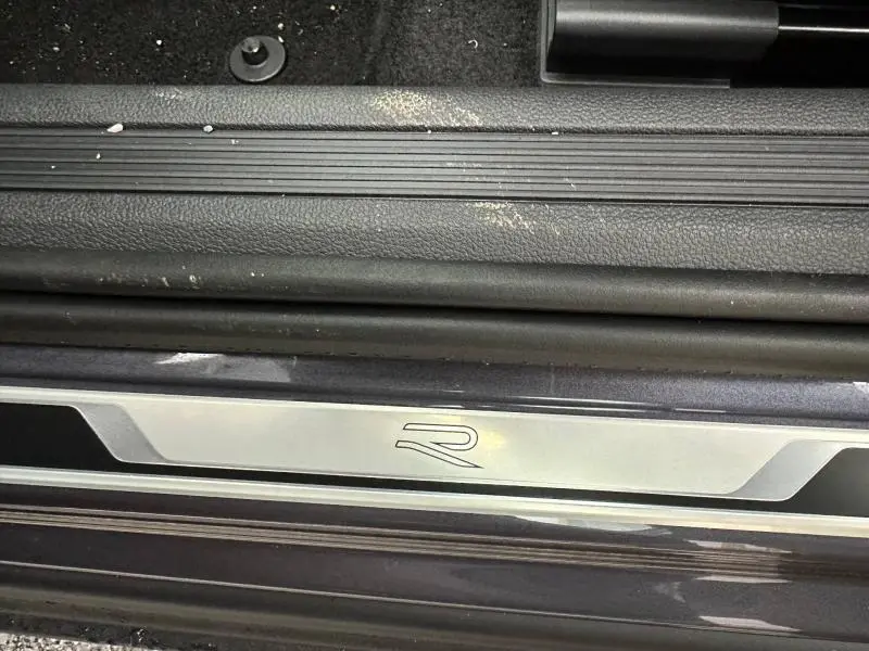 Gros plan sur la plaque de seuil de porte avec logo R du Volkswagen T-Cross Gris Ascot, version R-Line 2025.