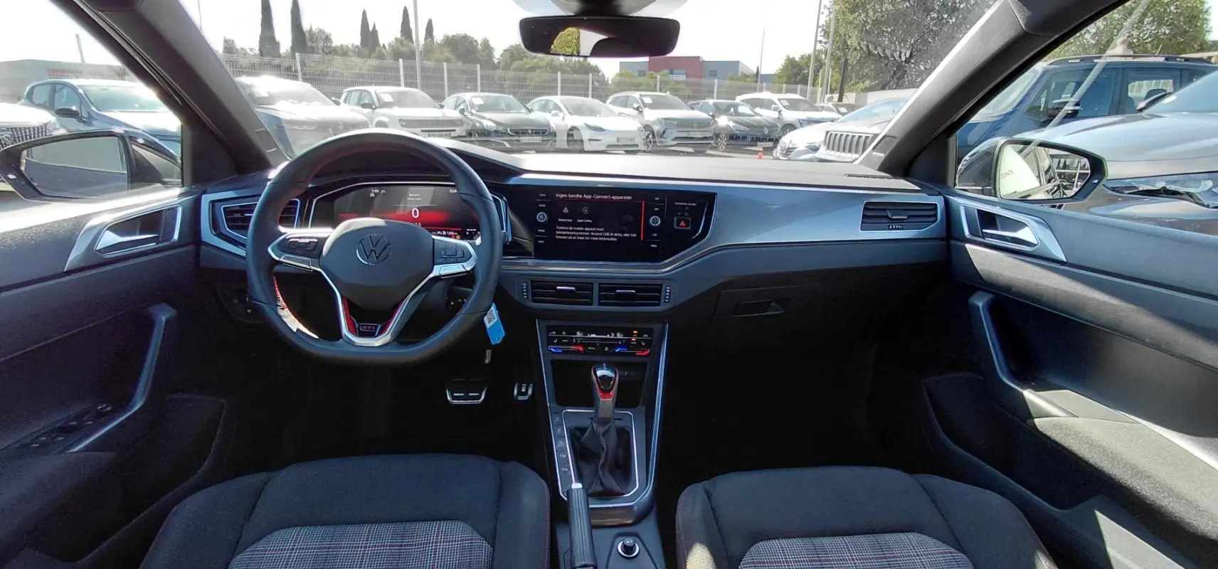 Vue intérieure avant de la Volkswagen Polo GTI 2024 noire, avec volant sport, écran tactile et levier de boîte automatique.